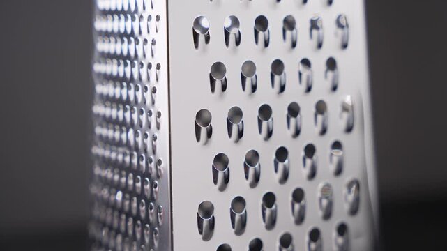 Rotating view of a stainless steel box grater showing multiple grating surfaces and polished metal finish. The slow rotation emphasizes functionality, symmetry, and professional kitchen quality.