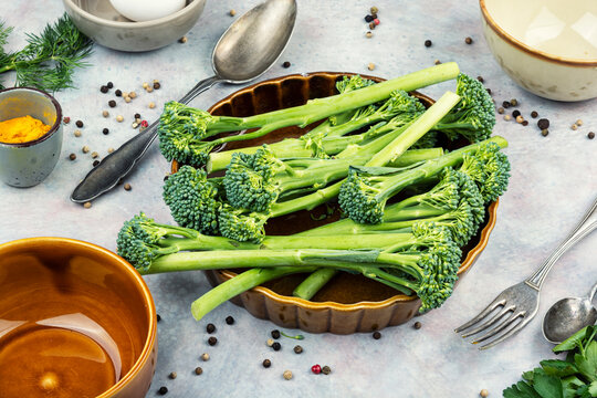 Raw broccolini prepared for clean kitchen surface with seasonings.
