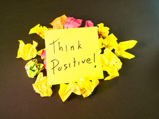 Think Positive! Motivation Note - Uplifting 'Think Positive!' message on a bright yellow note, contrasting with colorful crumpled paper on dark. Symbolizes optimism and resilience.