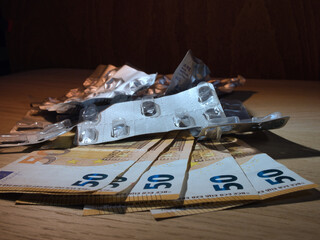 Medicine Costs: Empty Blisters, Euros - Empty pill blister packs and 50 Euro banknotes illustrate the high cost of medication and healthcare expenses in Europe, with copy space on wood.