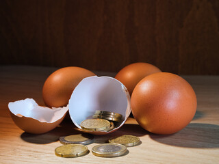 Money in Eggshell: Financial Nest Egg - Close-up of euro currency inside a broken chicken egg, with other eggs and coins on a rustic wooden surface. Concept of future savings and investment.