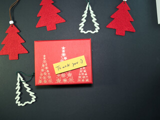 Christmas Gift Box with Thank You Note - Overhead shot of a red Christmas gift box featuring a 'Thank You' sticky note, festive tree decorations, and copy space on a dark background.