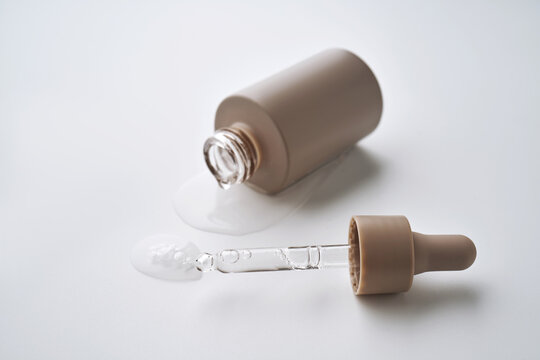 Skincare serum dropper bottle spilling liquid on white background
