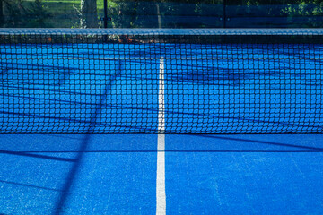 View of a padel court with open doors and bright blue playing surface in the afternoon sun