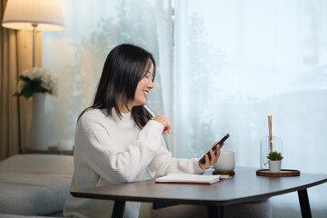Smiling young woman sitting at a table at home while looking at her smartphone.