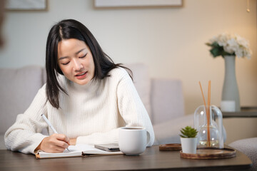 Smiling young woman writing in a journal while sitting in a cozy living room.