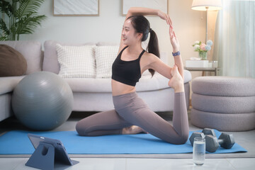 Female practicing gentle yoga at home while following an online class on a tablet. Self-care, home exercise, and wellness lifestyle.