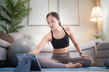 Woman exercising at home on a yoga mat, following an online workout on a tablet. Home fitness, digital training, and healthy lifestyle concept.