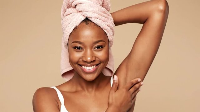 Beautiful Black woman with towel on head, arm raised, smiling. Beige background