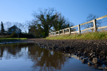 Fototapeta premium Reflection in a puddle of small village houses and wooden fence in winter under blue sky