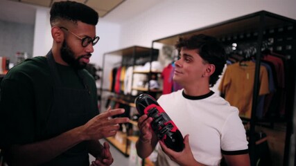 Knowledgeable shop assistant providing professional advice to a young man selecting new cycling shoes in a specialized sports equipment store, discussing features and fit for optimal performance