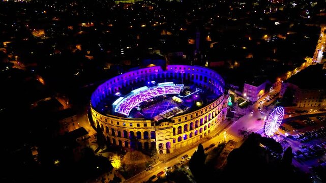 Aerial view of the ancient Pula Arena illuminated with vibrant purple and orange lights, showcasing a festive night event in Croatia.