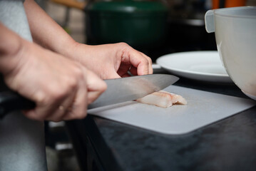 Hands guides a sharp knife over fish fillet on a white cutting board, a woman is cutting a fish fillet and is about to fry the fish at home