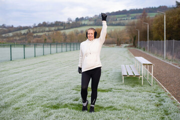 Woman celebrating victory on Frosty field in hoodie and earmuffs outdoors in winter. Woman beats her own record in sprinting and is now celebrating