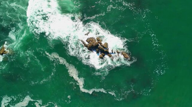 Birds-eye aerial drone view over greenish ocean with white foam waves and rocks, camera moving down, Portugal