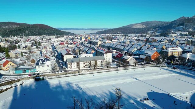 Aerial view of a snow-covered Delnice nestled in a mountain valley under a clear winter sky, showcasing pristine natural beauty and urban life.