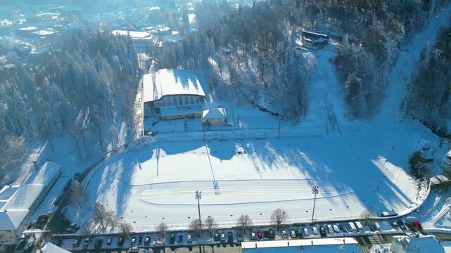 Aerial view of a snow-covered Delnice nestled in a mountain valley under a clear winter sky, showcasing pristine natural beauty and urban life.