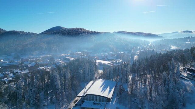Aerial view of a snow-covered Delnice nestled in a mountain valley under a clear winter sky, showcasing pristine natural beauty and urban life.