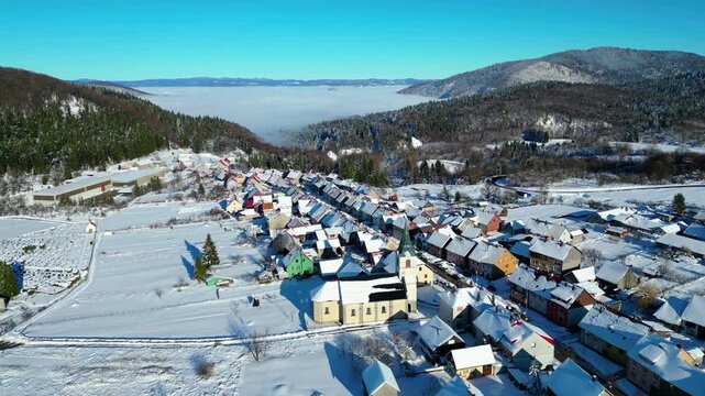 Aerial view of snow-covered Delnice, Croatia, nestled in a valley with a distant cloud inversion. Winter landscape under a clear blue sky. Perfect for winter travel.