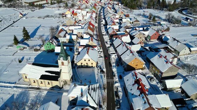 Winter's embrace in a charming Croatian village Delnice, with snow-dusted roofs and a prominent church under a clear blue sky. Fog blankets the distant valley.