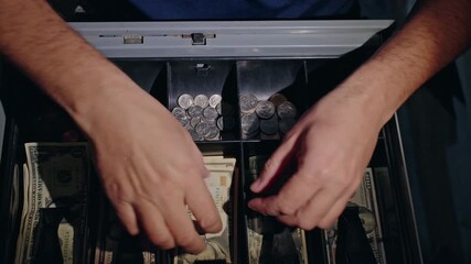 Cashier hands placing US dollar banknotes into cash register while giving change to customer, close up view of retail payment process with American currency and coin tray