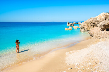 Unidentified young woman in swimsuit taking picture of amazing Megali Petra beach with turquoise sea and rocks, Lefkada island, Greece