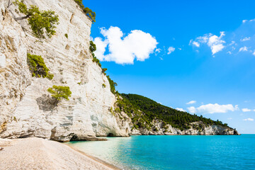 Majestic white limestone cliffs towering over a quiet pebble Vignanotica beach on the Gargano coast, Apulia, Italy
