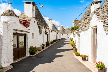 Peaceful trulli-lined street with stone paths and colorful potted plants basking in sunlight in Alberobello town, Apulia, Italy
