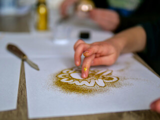Child&rsquo;s Fingers Touching Gold Glitter on a Paper Craft Project - DIY Holiday Art: A Child Creating a Sparkly Design with Gold Glitter and Glue