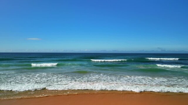 Low aerial drone flight from beach toward ocean with rising camera and waves, Portugal