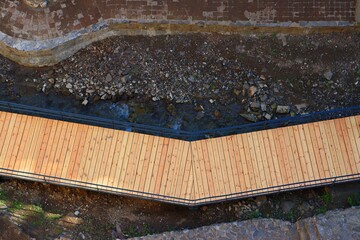 A pedestrian wooden bridge along a mountain stream between steep cliffs, view from above