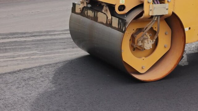 Heavy machinery is at work as roller compacts freshly laid asphalt on construction site
