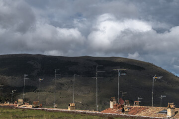 Dachlandschaft mit Antennen vor bewaldetem Berg und Gewitterwolken