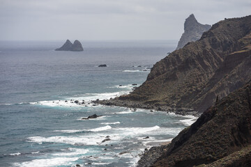 Rocky Atlantic coastline with dramatic cliffs, ocean waves, and distant volcanic islets near Benijo beach, Tenerife, Canary Islands, Spain.