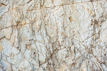 Close-up texture of rugged light gray volcanic rock surface with cracks, fissures, and subtle yellow mineral deposits as natural background.