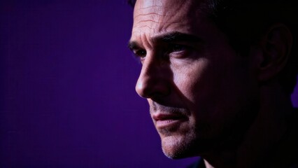 Obraz premium Dramatic of a serious adult man's face in profile highlighted by high-contrast side lighting on a vibrant purple background.