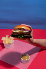 Isolated Beef Burger in Hand on Vibrant Blue Background