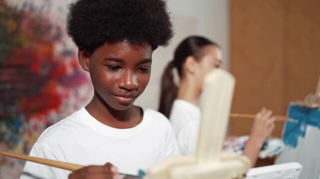 Smart african boy painting canvas while cute girl drawing behind. in art lesson. high school student create artwork by express creativity idea while standing at colorful stained wall. Edification