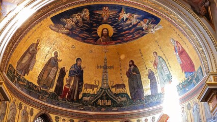 Rome, Italy &ndash; 14 January 2025. In San Giovanni in Laterano, a golden apse mosaic features Christ above a cross, flanked by saints, Mary, and John the Baptist, with symbolic animals and lush ground