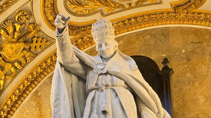 Rome, Italy &ndash; 14 January 2025. In San Giovanni in Laterano, a marble statue of a pope with tiara and robes raises his hand in blessing beneath golden detailing and symbols of the papacy.