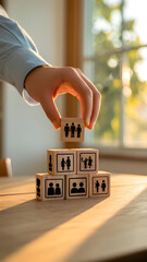 Hand Placing Wooden Cube on Pyramid of Social and Family Icon Blocks