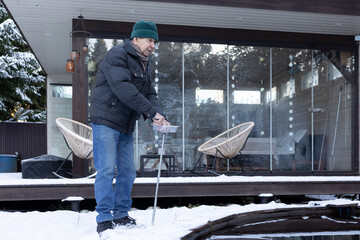 Male person near water pond throwing food to fish on snow covered landscape. Peaceful lifestyle moment on natural light scene.