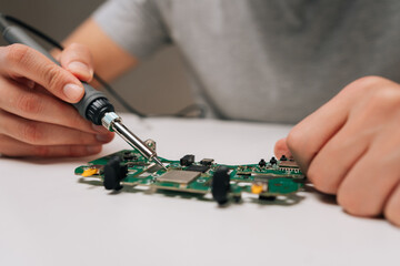 Close-up of repairman holding soldering iron, repairing game controller circuit board, performing electrical maintenance, working on electronic component repair, diy project on white table.