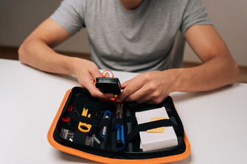Person handling multimeter and organizing various small tools inside compact orange and black zippered case, preparing for or performing electronics repair and assembly tasks.