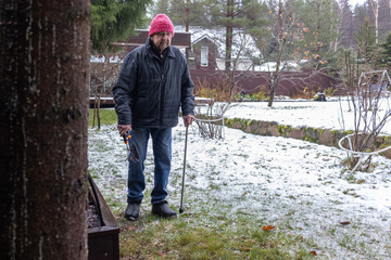 Elderly male maintaining plants in garden box during early winter. Casual outdoor labor on residential yard environment.