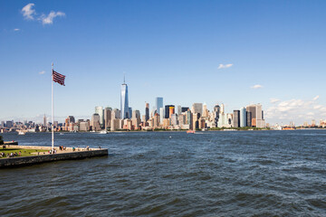 Flag of America fluttering in the breeze on Ellis Island with New York unmistakeable and iconic Manhattan cityscape in background across the Hudson