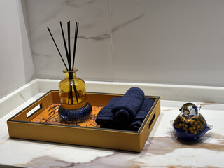 Bathroom counter with a reed diffuser, rolled towels, and a glass bird figurine on a marble countertop. © Ray