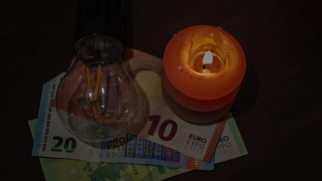 A burning candle and an unplugged lamp lie on banknotes. Power outages due to the war in Ukraine.