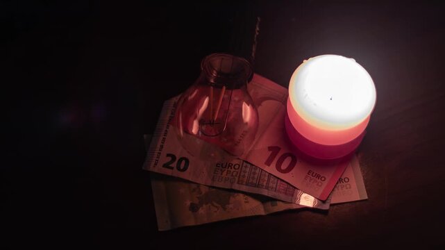 A burning candle and an unplugged lamp lie on banknotes. Power outages due to the war in Ukraine.