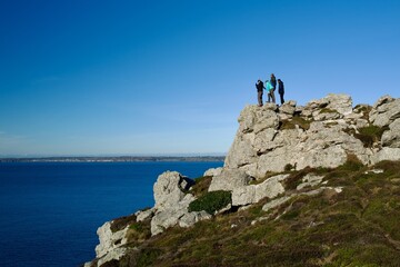 Three hikers on a rocky sea cliff under clear blue sky &mdash; adventure, freedom and achievement with copy space